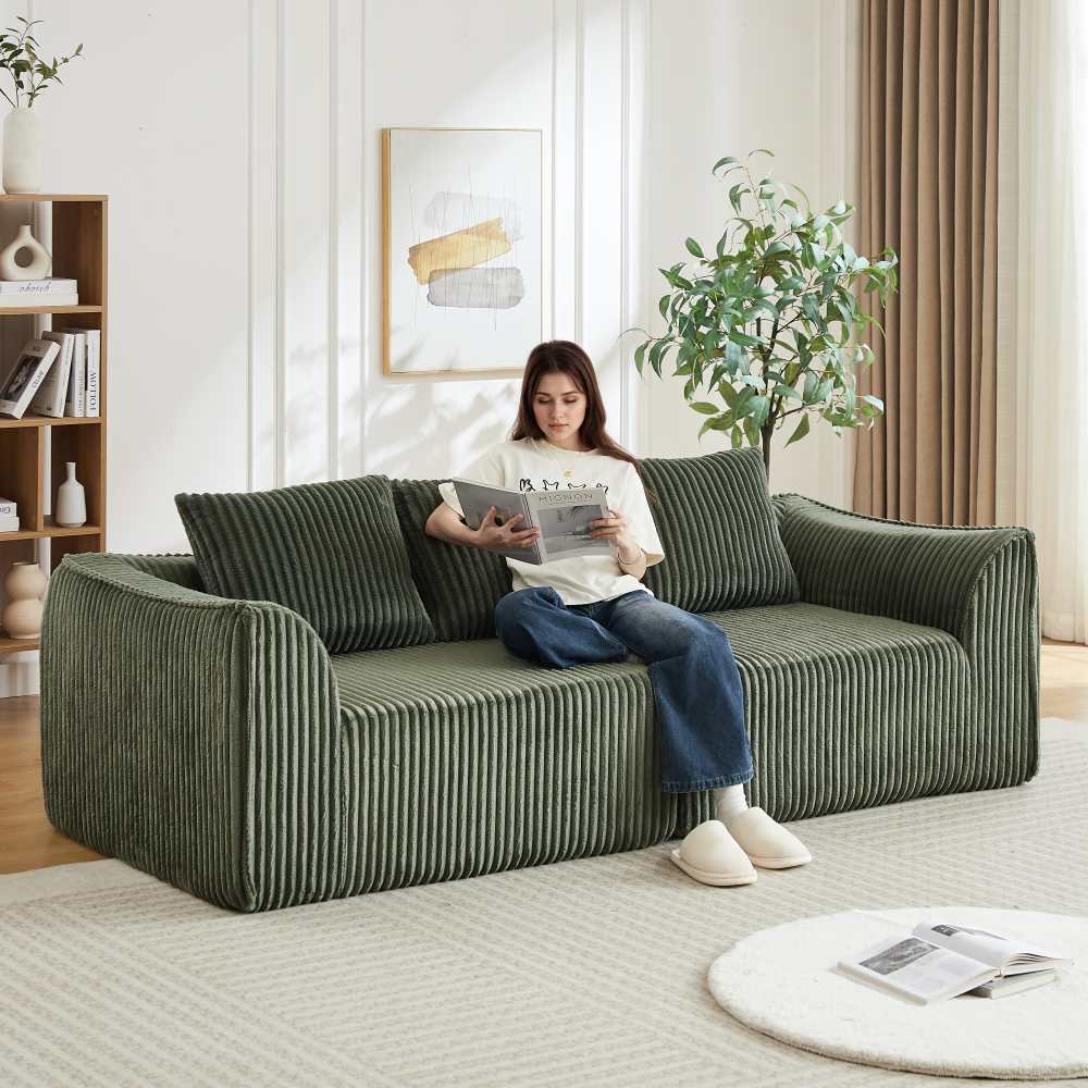 Minimalistyczna sofa z kordu o zaokrąglonych liniach i lekko pochylonym oparciu, w komplecie z dwiema poduszkami.