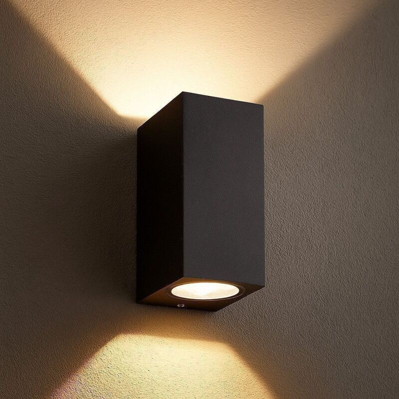 Czarna, prostokątna lampa ścienna zewnętrzna – wykonana z trwałego odlewu aluminiowego – do montażu na ścianie.